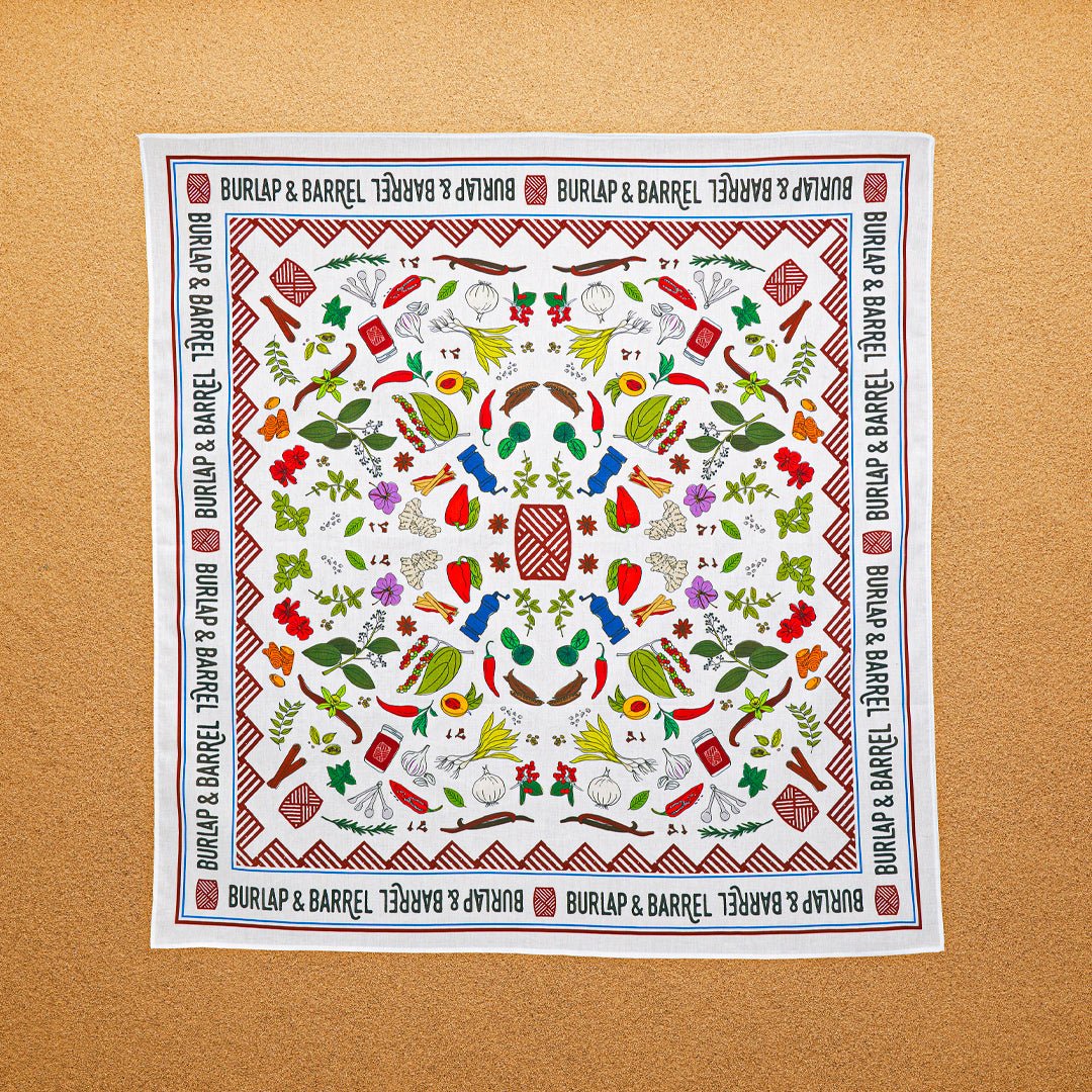 A multicolored, 100% cotton bandana with hand-drawn spice illustrations laid out flat on a surface.