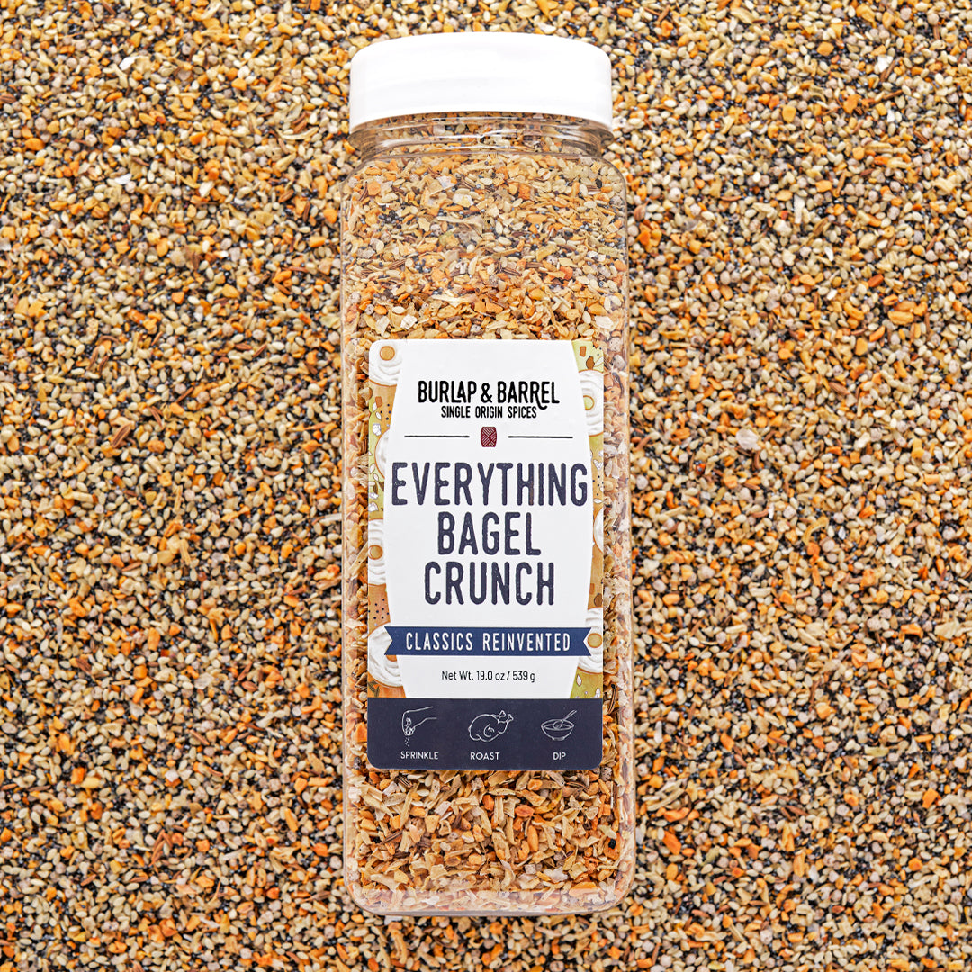 Container of Everything Bagel Crunch Seasoning from Burlap & Barrel on a bed of seeds and spices.
