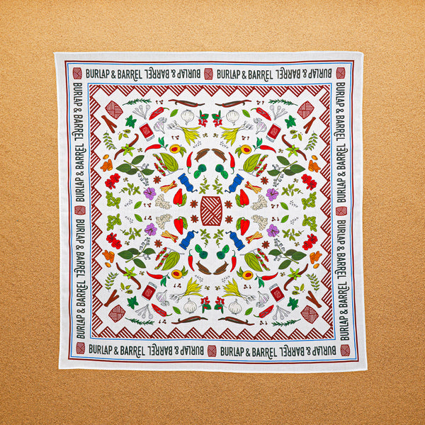 A multicolored, 100% cotton bandana with hand-drawn spice illustrations laid out flat on a surface.