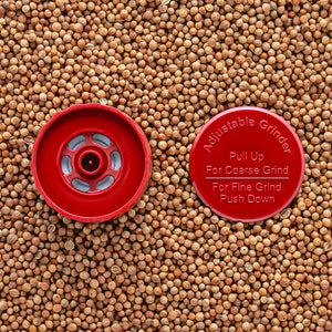 A red adjustable grinder top placed on a background of seeds, with instructions 'Pull Up For Coarse Grind' and 'Push Down For Fine Grind' visible.