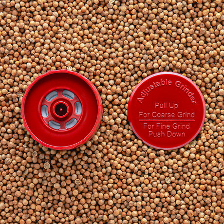A red adjustable grinder top placed on a background of seeds, with instructions 'Pull Up For Coarse Grind' and 'Push Down For Fine Grind' visible.