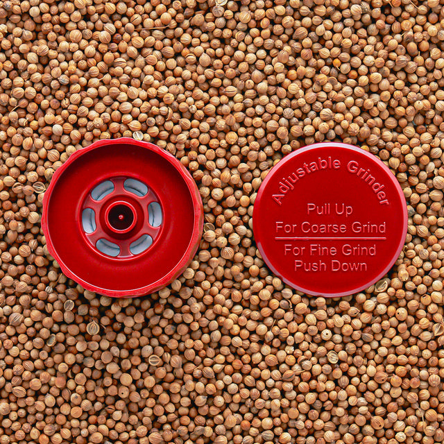 A red adjustable grinder top placed on a background of seeds, with instructions 'Pull Up For Coarse Grind' and 'Push Down For Fine Grind' visible.