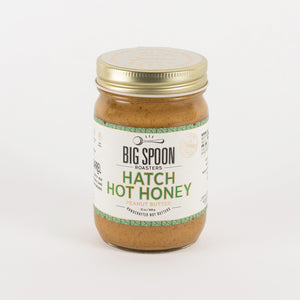 A jar of Big Spoon Roasters Hatch Hot Honey in garlic butter flavor, featuring a white label with green text and a gold metal lid, set against a plain white background.