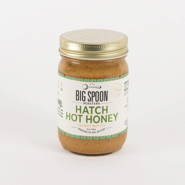 A jar of Big Spoon Roasters Hatch Hot Honey in garlic butter flavor, featuring a white label with green text and a gold metal lid, set against a plain white background.