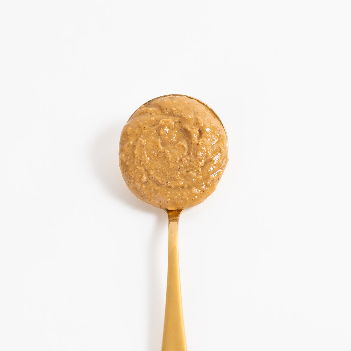 A close-up of a round, textured golden-brown peanut butter, spread evenly on a gold spoon against a clean white background