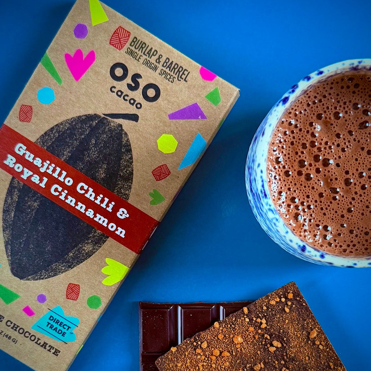 Oso Cacao guajillo chili & royal cinnamon chocolate bar packaging with a cup of hot chocolate on a blue background. Made with Burlap & Barrel spices.