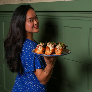 Woman in a blue dress holding a plate of food against a green wall.