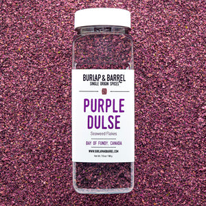 A container of Purple Dulse Flakes by Burlap & Barrel, sustainably hand-harvested from the Bay of Fundy, Canada, displayed on a background of dulse flakes.