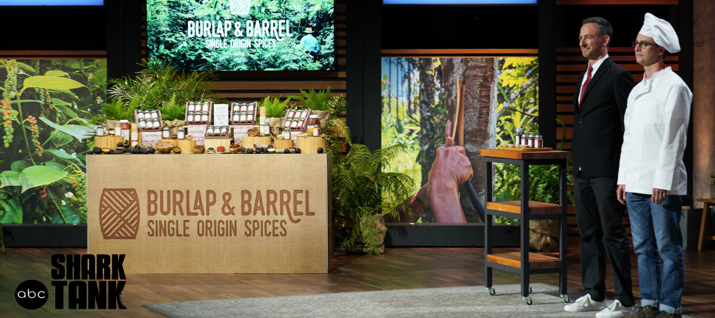 Ethan & Ori, Co-founders of Burlap & Barrel on the Shark Tank stage with a display of Burlap & Barrel spices. Ethan is wearing a chef's hat and Ori is wearing a suit. 