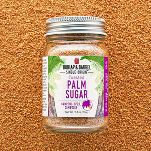 A glass jar of Burlap & Barrel Toasted Palm Sugar, featuring a white and purple label with green palm leaf graphics, sealed with a silver metal lid and set against a textured brown background.
