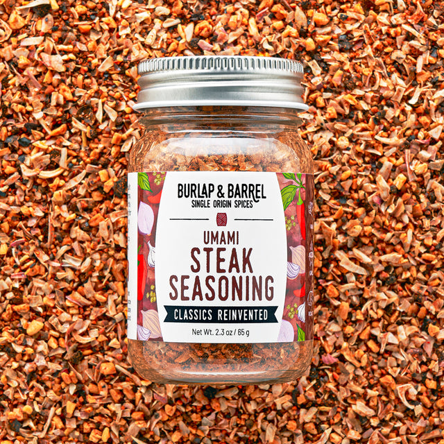 Jar of Burlap & Barrel Umami Steak Seasoning on a background of spices