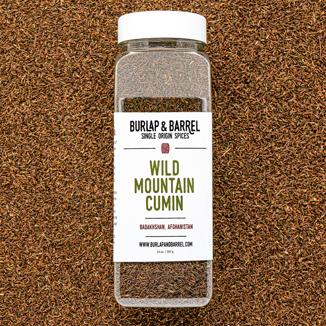 Plastic container of wild mountain cumin from Burlap & Barrel on a background of loose cumin seeds.