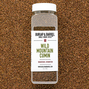 Plastic container of wild mountain cumin from Burlap & Barrel on a background of loose cumin seeds.