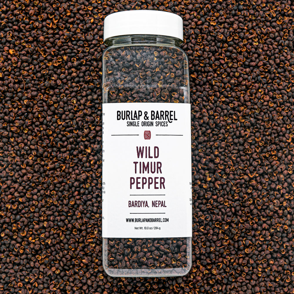 A bottle of Wild Timur Pepper by Burlap & Barrel, with the label showing the product name and origin, amidst loose peppers.