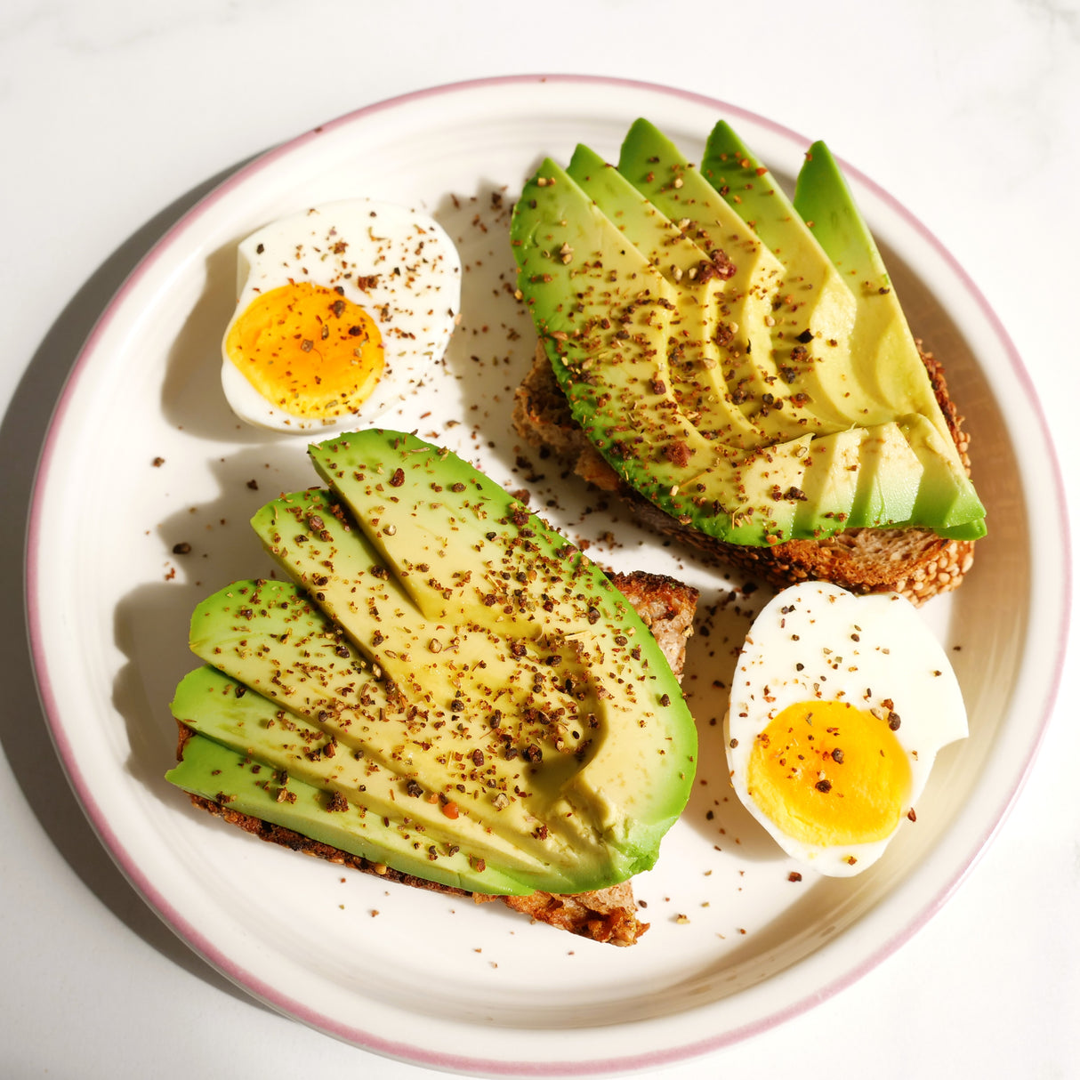 Avocado slices and boiled eggs on toast on a white plate with a pink rim.