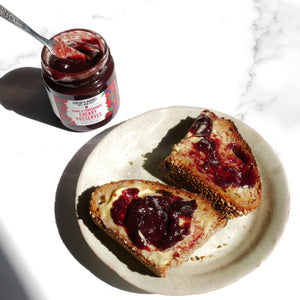 Two slices of toast with cherry preserves on a plate next to a jar of cherry preserves.